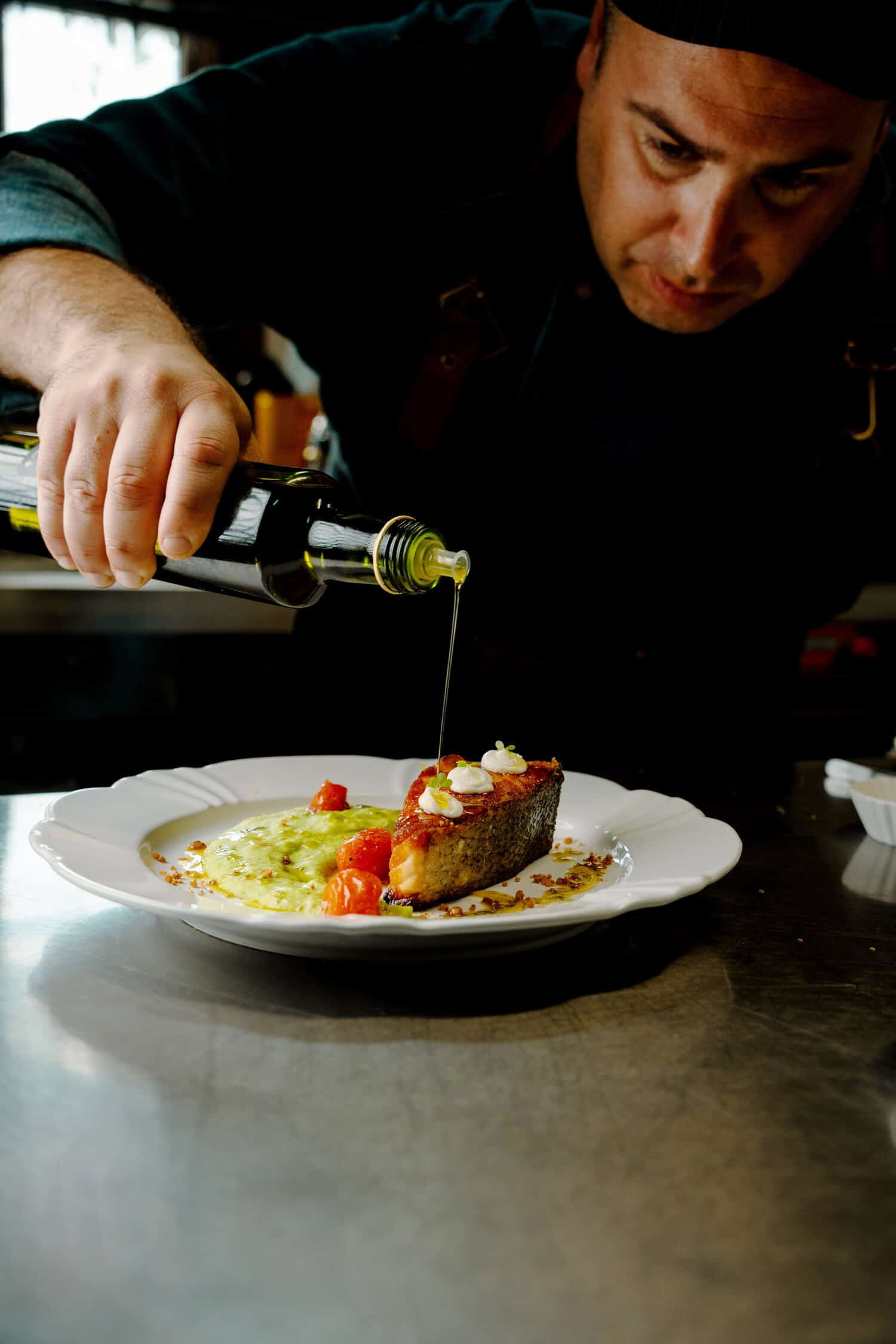 The chef of Sete Ais Bistro at Quinta das Videiras Hotel drizzling olive oil over a dish.